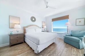 A bedroom with a bed, nightstands, a chair, a window with a view, and a ceiling fan.