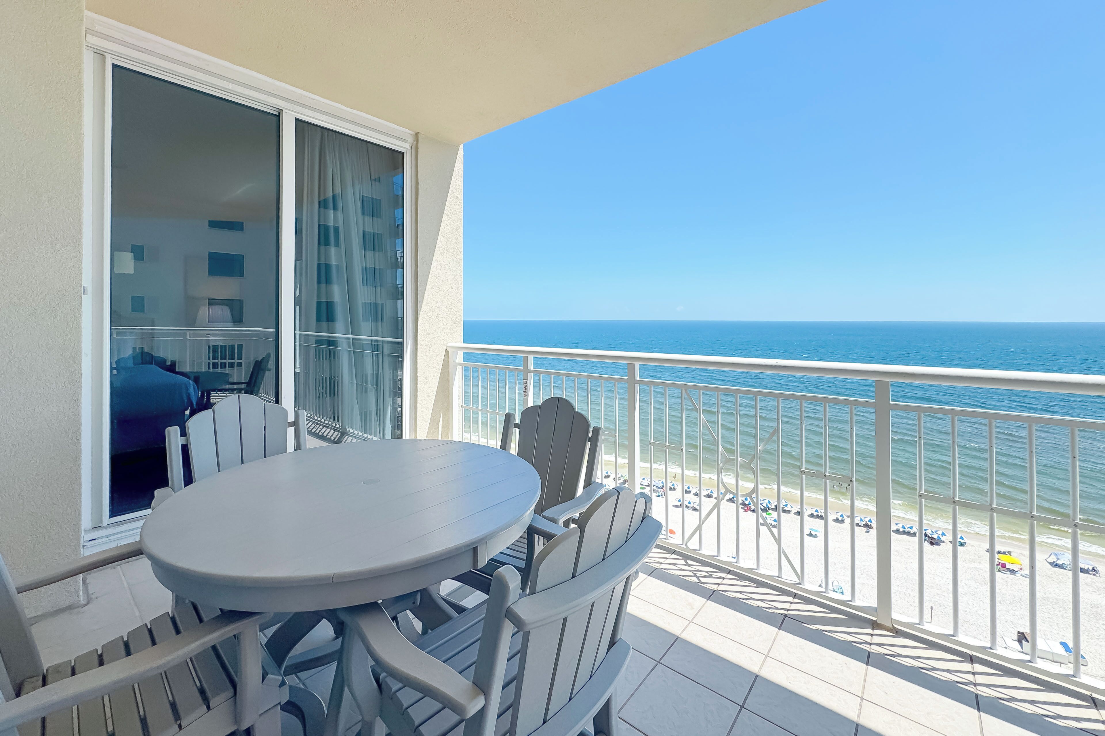 Ein Balkon mit Tisch und Stühlen, mit Blick auf einen Strand mit Sonnenschirmen und freier Meerblick.