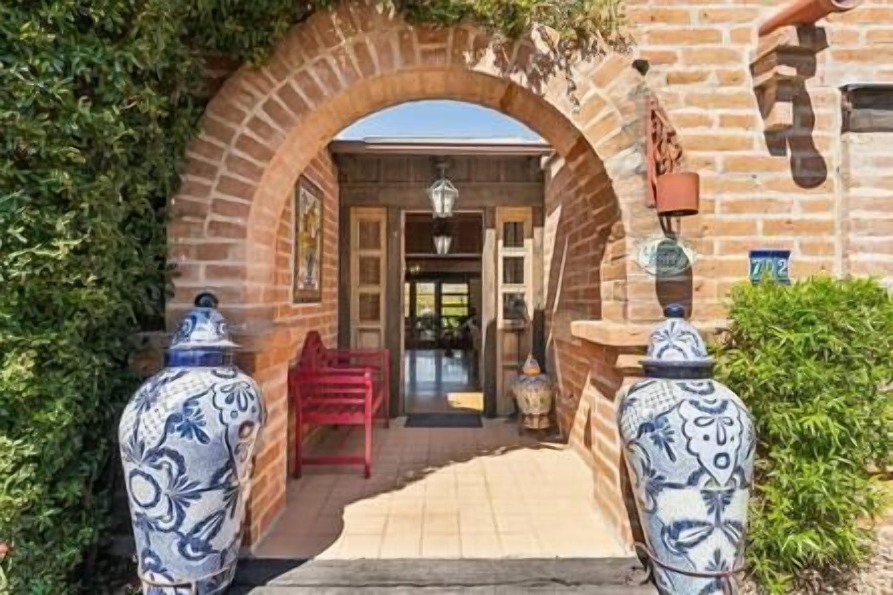 An entrance with a brick archway, a red chair, and two decorative vases.