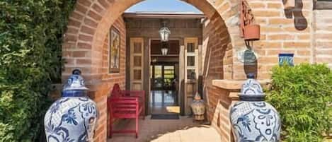 An entrance with a brick archway, a red chair, and two decorative vases.