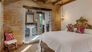 A bedroom with a large bed, a wooden headboard, a bedside table, a chair, and a bathroom visible through an open door.
