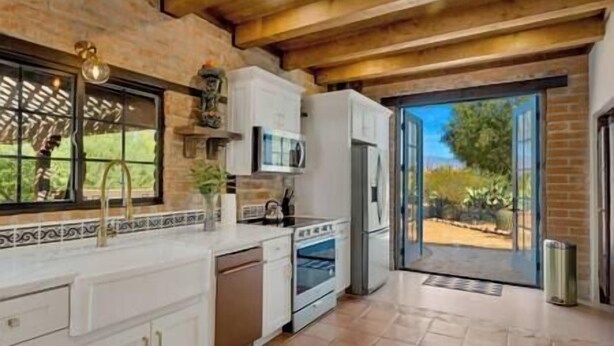 A kitchen with white cabinets, a built-in oven, and a large window overlooking a garden.