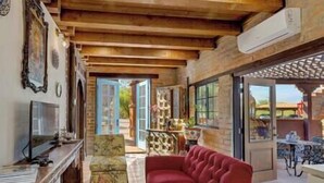 A cozy living room with a red sofa, wooden ceiling beams, a television, and a view through the glass door.