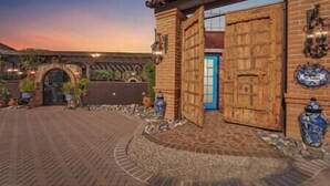 A courtyard with a brick pathway leading to a wooden gate, a blue door, and decorative vases.