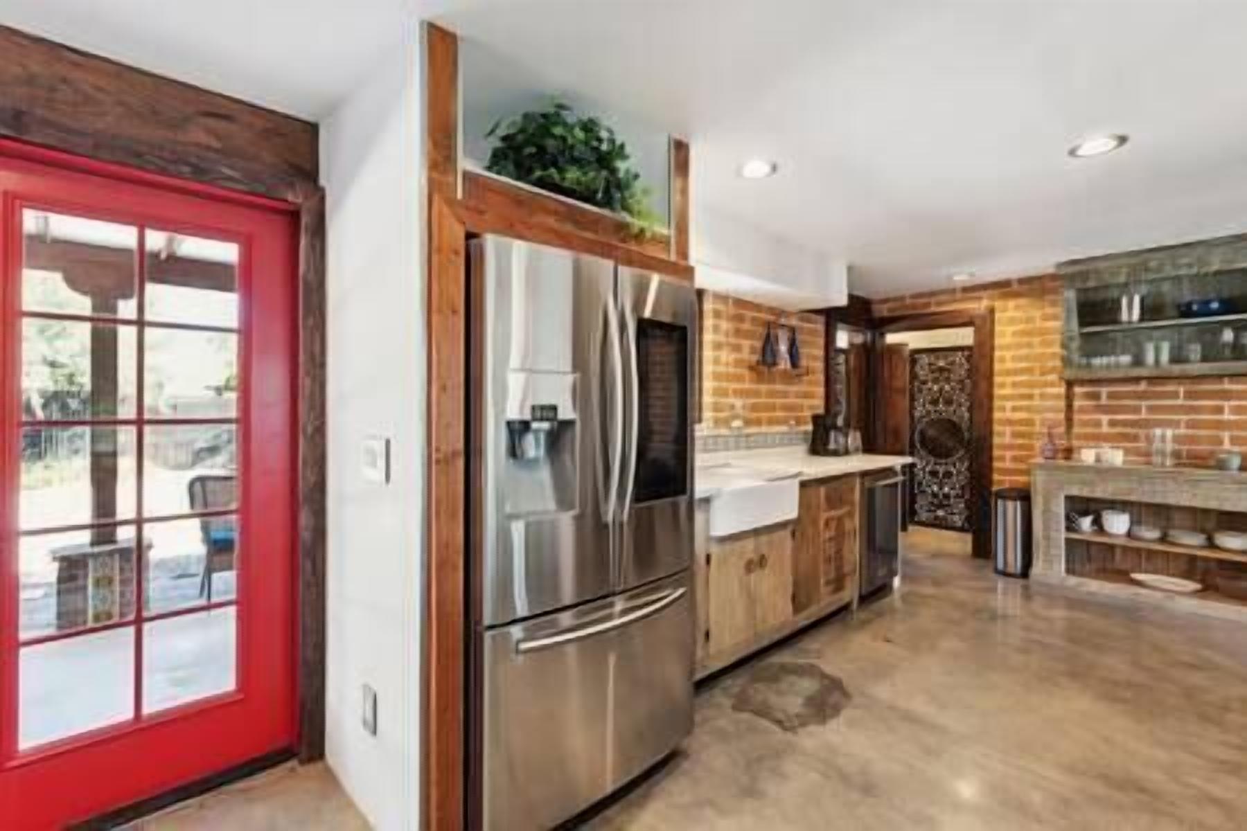 A modern kitchen with stainless steel appliances, wooden cabinets, and a red door.