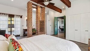 Une chambre dotée d’un grand lit, d’un ventilateur de plafond, de poutres apparentes et d’une cheminée en briques.