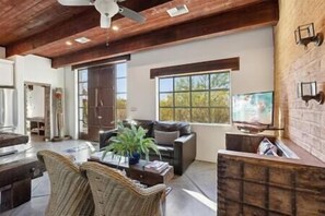 A spacious living room with a high ceiling, a fireplace, a television, and a large window.
