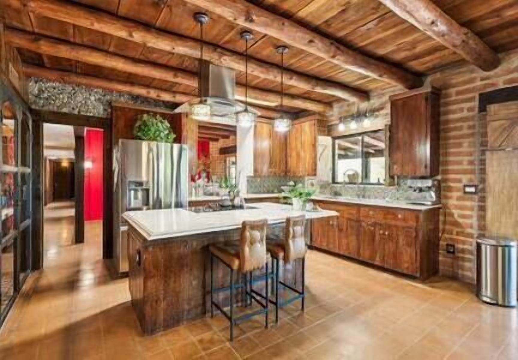 A spacious kitchen with a central island, wooden ceiling beams, and a stone accent wall.