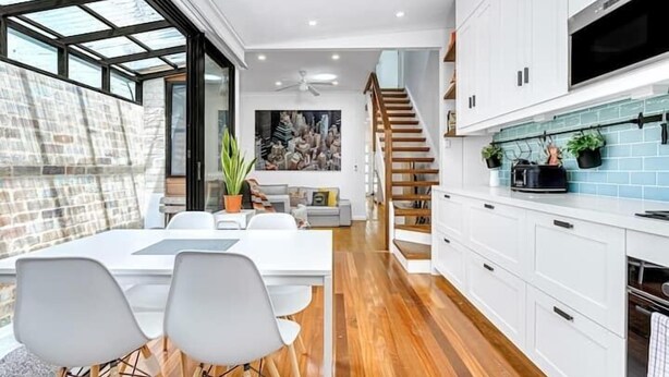 Una cocina moderna con armarios blancos, un salpicadero azul y una escalera de madera.