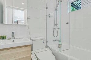 A modern bathroom with a glass shower enclosure, a white toilet, and a large mirror above the sink. - The Newtown Nest (Newtown)