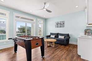 A room with a foosball table, a sofa, a round coffee table, and a ceiling fan.