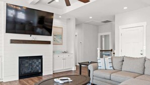 A living room with a fireplace, a television mounted on the wall, a sofa, and a coffee table. - Isle Escape by Brunswick Vacation Rentals: Pool, Elevator & Stunning Ocean Views (Ocean Isle Beach)