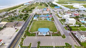 A coastal town with a large blue-roofed sports facility, a main road, and residential buildings. - Isle Escape by Brunswick Vacation Rentals: Pool, Elevator & Stunning Ocean Views (Ocean Isle Beach)