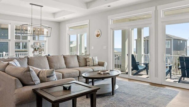 A spacious living room with a sectional sofa, a coffee table, and a ceiling fan. - Isle Escape by Brunswick Vacation Rentals: Pool, Elevator & Stunning Ocean Views (Ocean Isle Beach)