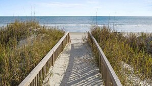 A wooden boardwalk leading to a beach with sand and grass on either side. - Isle Escape by Brunswick Vacation Rentals: Pool, Elevator & Stunning Ocean Views (Ocean Isle Beach)