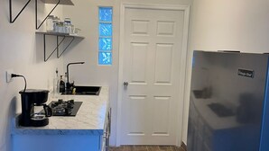 A compact kitchen with a built-in refrigerator, a coffee maker, and a window with blue-tinted glass panels. - DEPARTAMENTO PARA 5 (Ciudad Juárez)