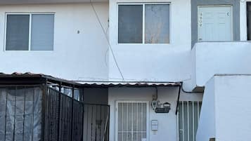 Un edificio de dos plantas con fachada blanca, una reja metálica y un pequeño porche.