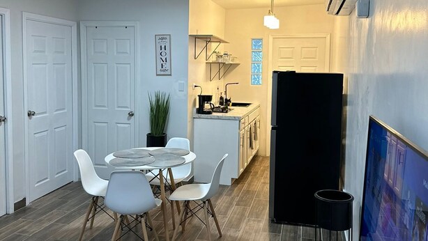 A modern kitchen with white cabinets, a black refrigerator, and a dining area with a round table and white chairs. - DEPARTAMENTO PARA 5 (Ciudad Juárez)