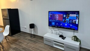 A modern living room with a flat-screen TV mounted on the wall, a white console table, a black floor lamp, and a black refrigerator. - DEPARTAMENTO PARA 5 (Ciudad Juárez)