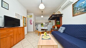 Een woonkamer met een televisie, een houten kast, een blauwe bank en een eethoek met een tafel en stoelen.