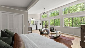 A spacious bedroom with a large bed, a seating area with a coffee table, and a view of the outdoors through large windows.