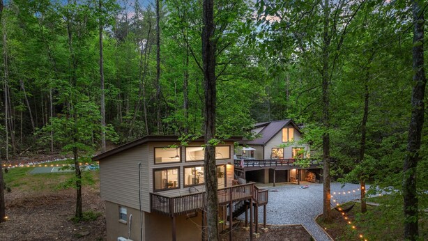 A two-story cabin with a deck and a covered patio area, surrounded by a forest.