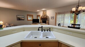 Una cocina con encimera blanca, doble pileta y chimenea de piedra.