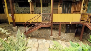 A rustic wooden building with a stone wall, a yellow exterior, and a metal staircase leading to a wooden deck. - Relax and Enjoy the Ocean Views-Breakfast Included (Uvita)