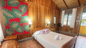 A wooden-paneled room with a bed, two bedside lamps, a large tropical leaf-patterned tapestry, and a small wooden stool. - Relax and Enjoy the Ocean Views-Breakfast Included (Uvita)