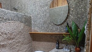 A bathroom with a stone wall, a wooden ceiling, a toilet, a sink with a mirror, and a small shelf with toiletries. - Relax and Enjoy the Ocean Views-Breakfast Included (Uvita)
