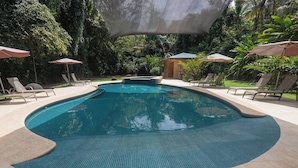 A swimming pool with tiled edges, surrounded by lounge chairs and umbrellas, set in a lush, green environment. - Relax and Enjoy the Ocean Views-Breakfast Included (Uvita)