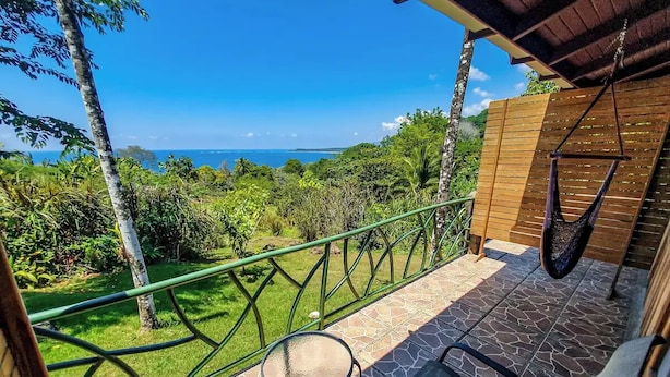 A balcony with a view of the ocean, a hanging chair, and a small table. - Relax and Enjoy the Ocean Views-Breakfast Included (Uvita)