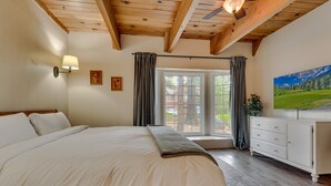 Een slaapkamer met een groot bed, houten balken in het plafond, een witte kapstok en een raam met gordijnen.