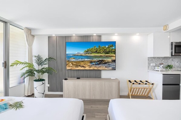 Ein modernes Hotelzimmer mit einem großen Fernseher, einer kleinen Küchenzeile, einer Holzbank und einem Topfpflanzen.