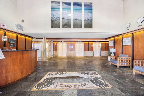 A hotel lobby with a reception desk, elevators, and a large window with a view of the ocean.