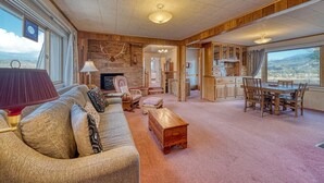 A spacious living room with a fireplace, a dining area with wooden furniture, and large windows offering a view of the countryside. - Casa Commodore ~ Paddles, Pups & Proximity! (Salida)