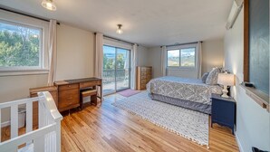 A bedroom with a wooden desk, a bed with a patterned bedspread, a nightstand with a lamp, and a view of the outdoors through a sliding glass door. - Casa Commodore ~ Paddles, Pups & Proximity! (Salida)