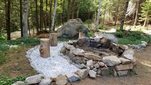 A forest scene with a stone fire pit surrounded by white pebbles and large rocks, with birch trees in the background. - Modern, 2 King, 4 BDRM Private Luxury Log Cabin, 5 Star, Family Friendly (Intervale)