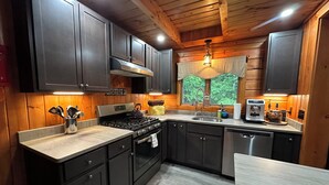 A modern kitchen with dark cabinets, a stainless steel stove, and a window with a view of trees. - Modern, 2 King, 4 BDRM Private Luxury Log Cabin, 5 Star, Family Friendly (Intervale)