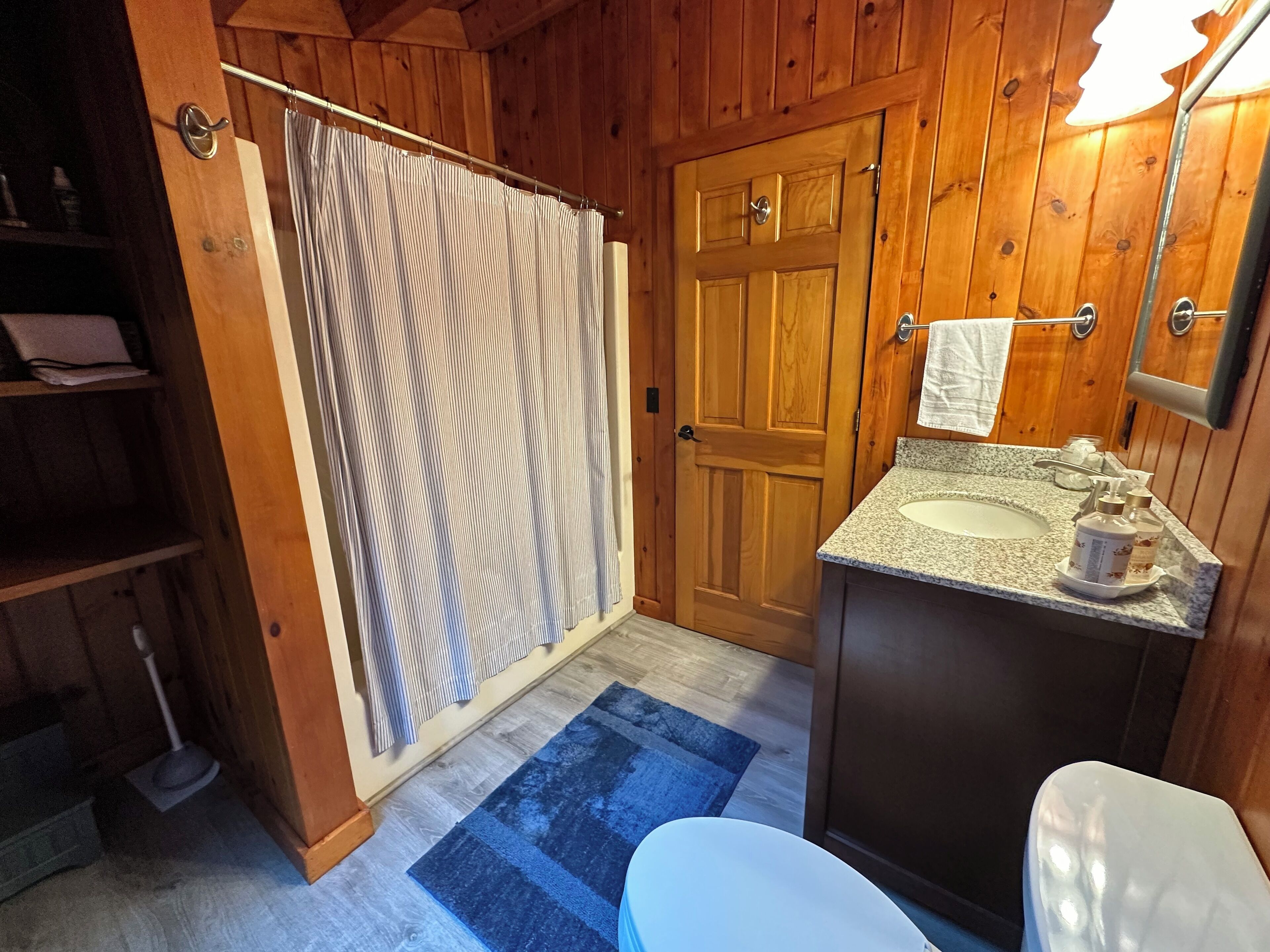 A wooden cabin bathroom with a shower curtain, a wooden door, a sink with toiletries, and a toilet.