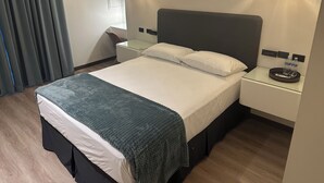 Una habitación de hotel moderna con una cama grande, dos mesitas de noche, una lámpara colgante y una cortina azul.