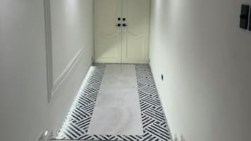 Un pasillo con piso estampado, paredes blancas y una puerta doble al final.