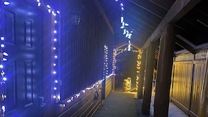 Um corredor com paredes de madeira e chão coberto de neve, iluminado por luzes de Natal.