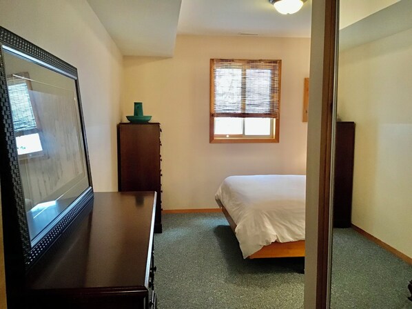 A bedroom with a bed, a dresser, a mirror, and a window with blinds.