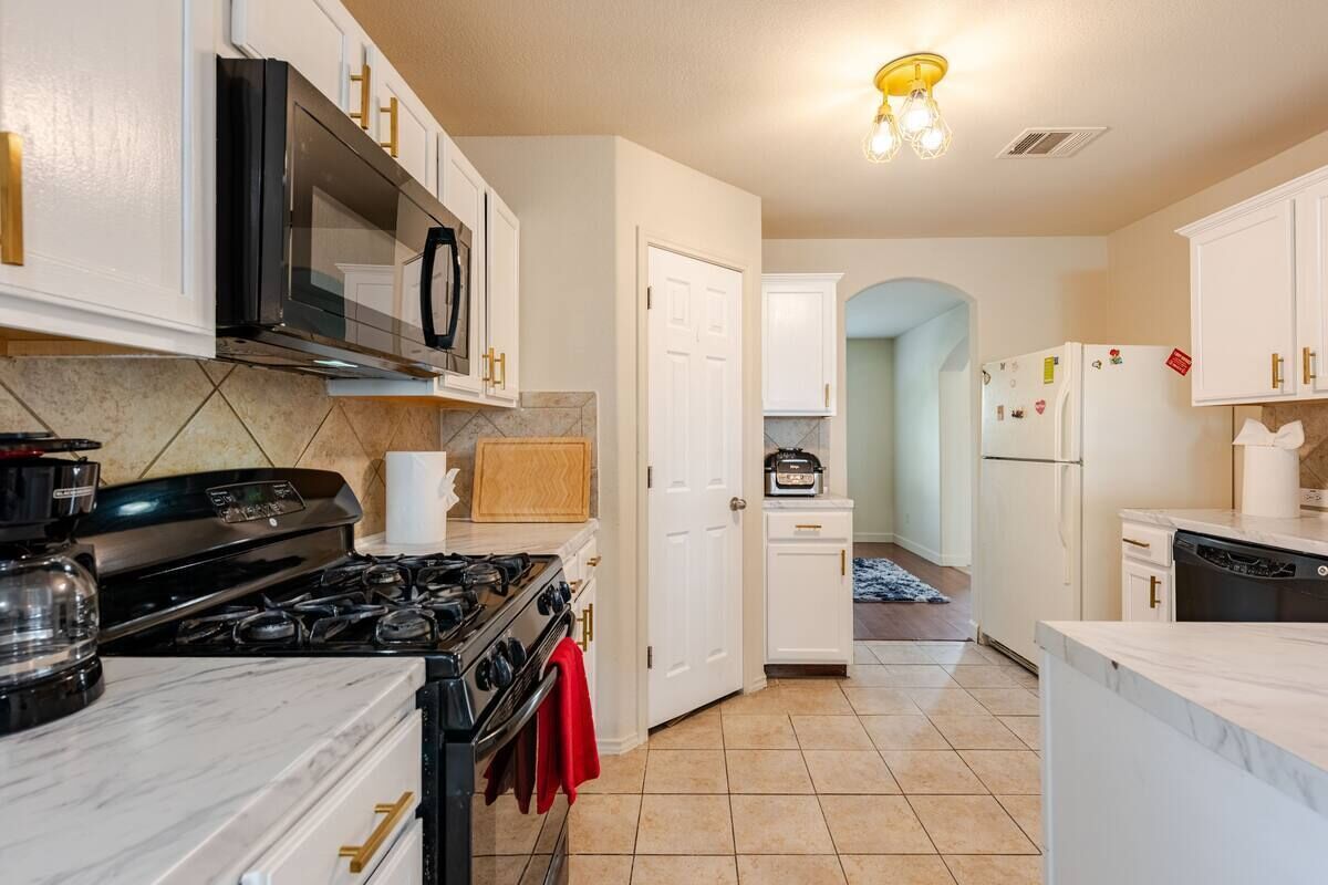 A kitchen with white cabinets, a black stove, a microwave, and a refrigerator.