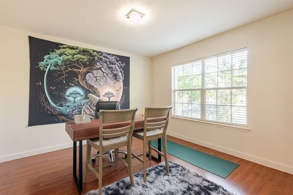 A dining area with a wooden table and chairs, a large abstract painting on the wall, a window with blinds, and a yoga mat on the floor. - Chic, Comfortable Home Steps from SXSW Fun (Buda)