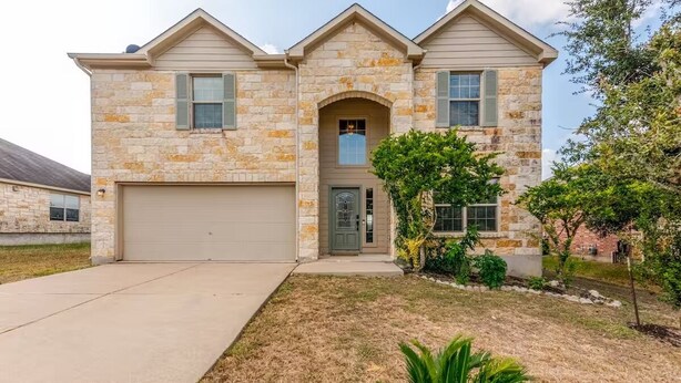 A two-story stone house with a garage, a front door, and a small front yard with a palm tree and shrubs. - Chic, Comfortable Home Steps from SXSW Fun (Buda)