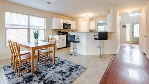 A modern kitchen with white cabinets, a central island, and a dining area with a wooden table and chairs. - Chic, Comfortable Home Steps from SXSW Fun (Buda)