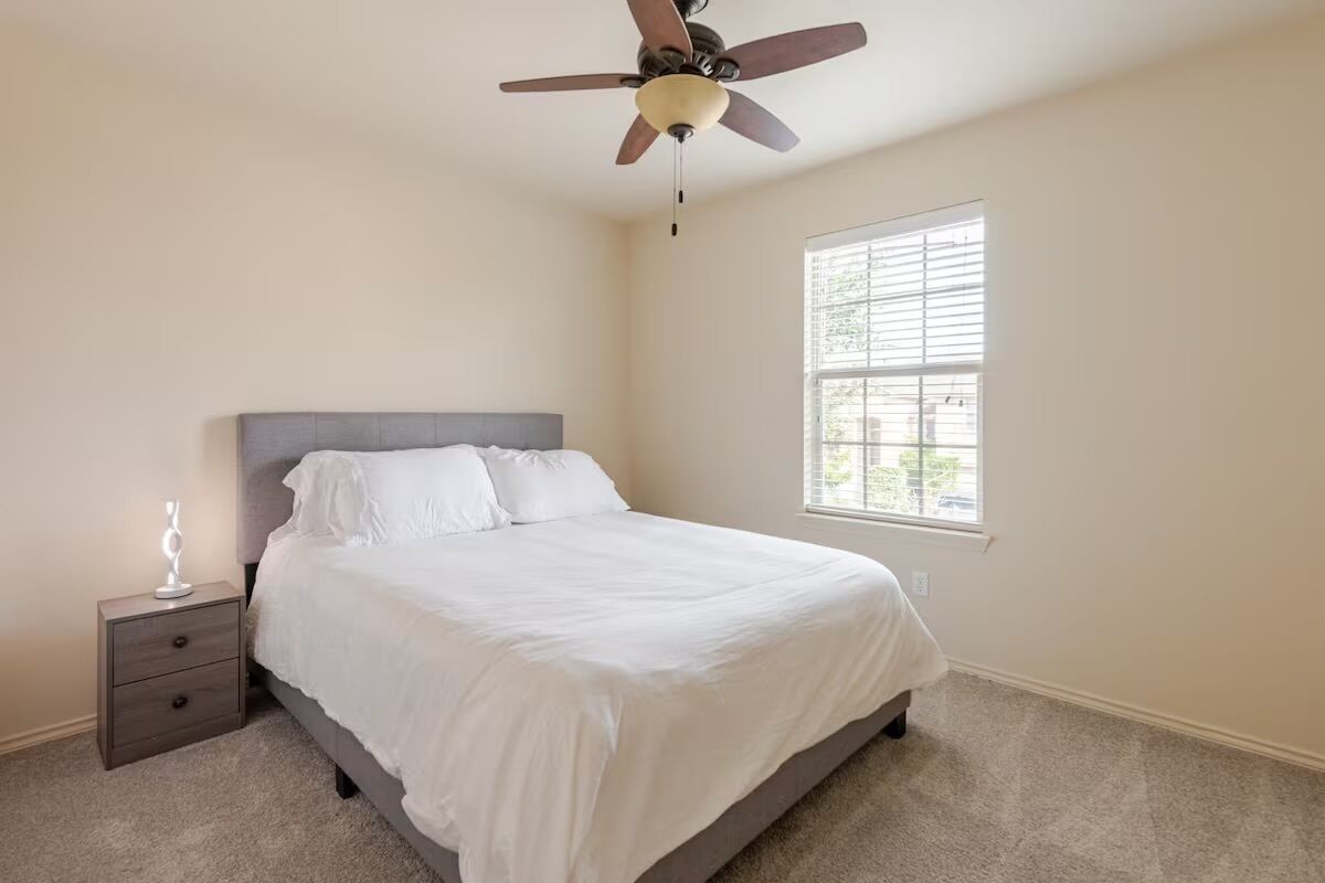 A bedroom with a bed, a nightstand, a ceiling fan, and a window.