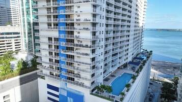 A high-rise hotel with multiple balconies, a swimming pool, and a view of the ocean.